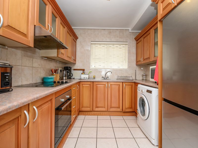 A functional kitchen featuring wooden cabinetry, laminate countertops, ceramic tile backsplash, and integrated appliances including an oven, hob, and extractor fan.