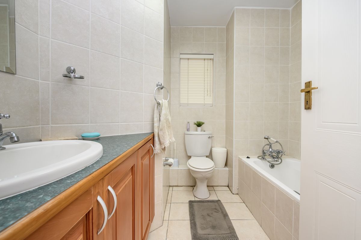 A functional bathroom featuring a vanity cabinet with a drop-in sink, a standard toilet, and a bathtub with a shower mixer, finished with neutral wall tiles.