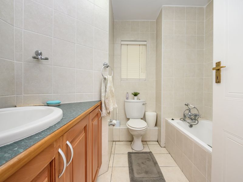 A functional bathroom featuring a vanity cabinet with a drop-in sink, a standard toilet, and a bathtub with a shower mixer, finished with neutral wall tiles.