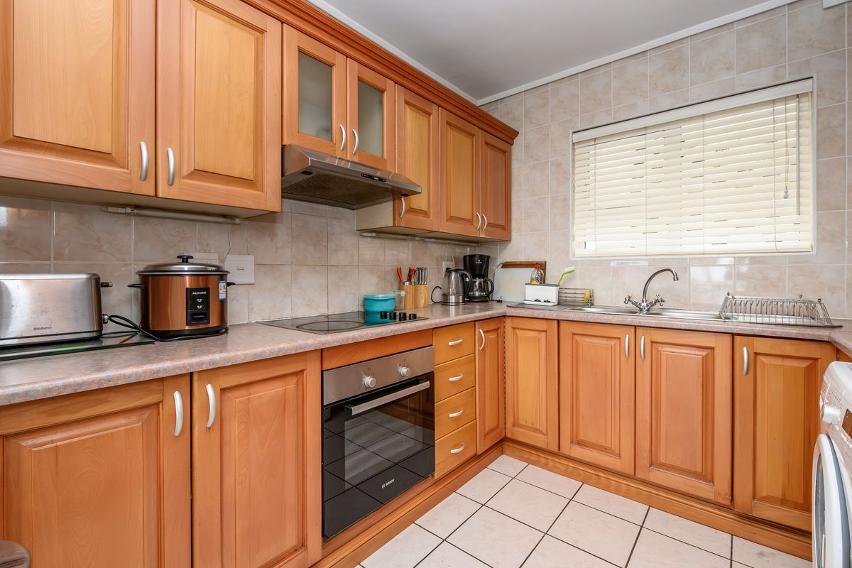 A functional kitchen featuring wooden cabinetry, laminate countertops, ceramic tile backsplash, built-in oven, electric hob, and a stainless steel sink with a window view.