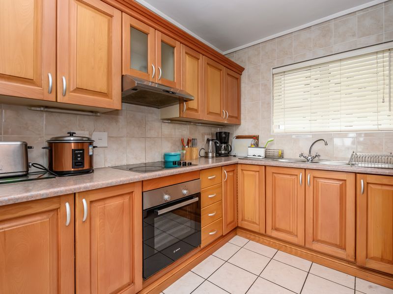 A functional kitchen featuring wooden cabinetry, laminate countertops, ceramic tile backsplash, built-in oven, electric hob, and a stainless steel sink with a window view.
