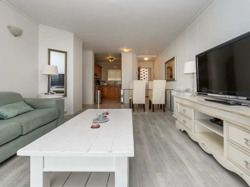 An open-plan living and dining area featuring light-toned laminate flooring, neutral walls, and a seamless transition into the kitchen space.