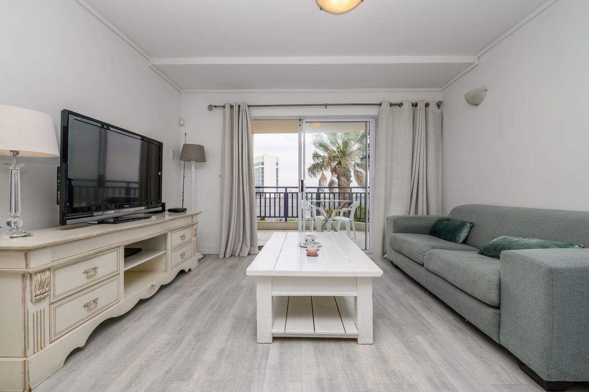 A bright living room featuring light-toned laminate flooring and a sliding glass door that opens onto a private balcony.