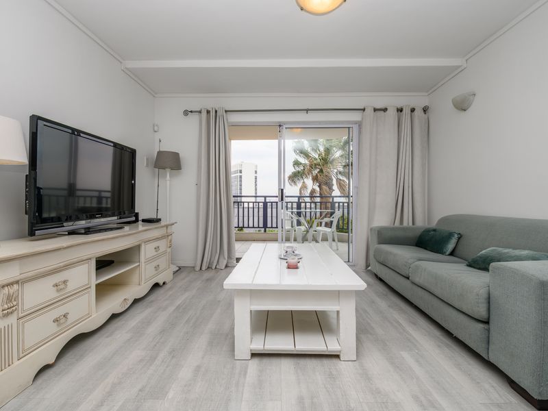 A bright living room featuring light-toned laminate flooring and a sliding glass door that opens onto a private balcony.