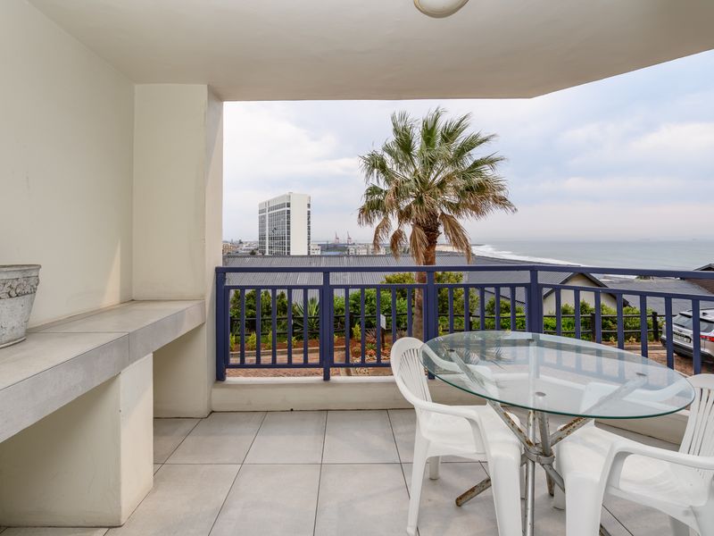 Covered balcony featuring a built-in concrete counter, tiled flooring, and a metal balustrade with scenic coastal and urban views.