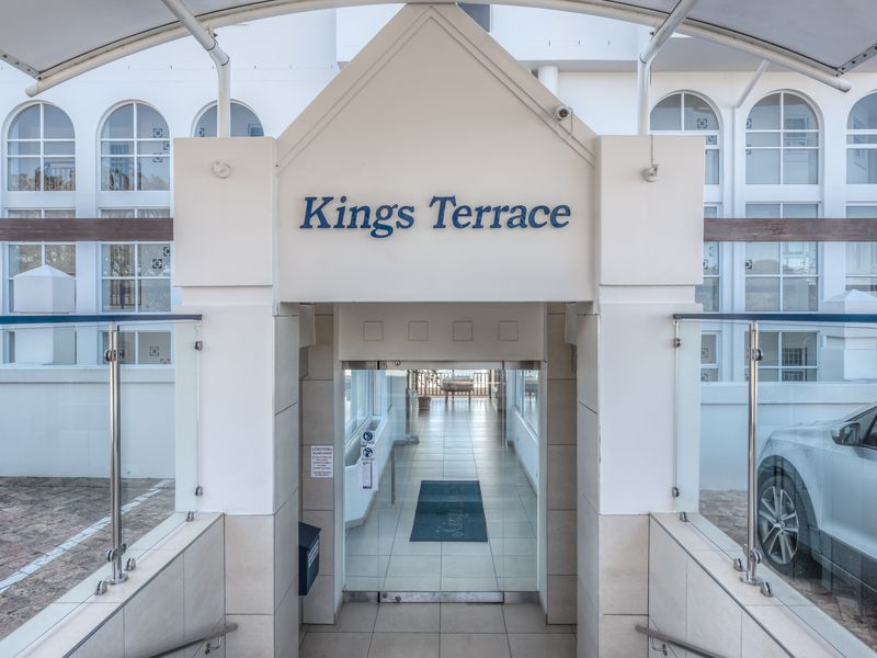 Main entrance to Kings Terrace apartment complex featuring a covered walkway, glass balustrades, and tiled flooring.