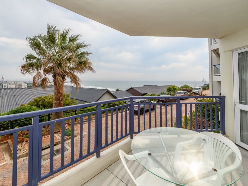 A covered balcony featuring tiled flooring and a blue railing, offering elevated views of the surrounding neighborhood and distant coastline.