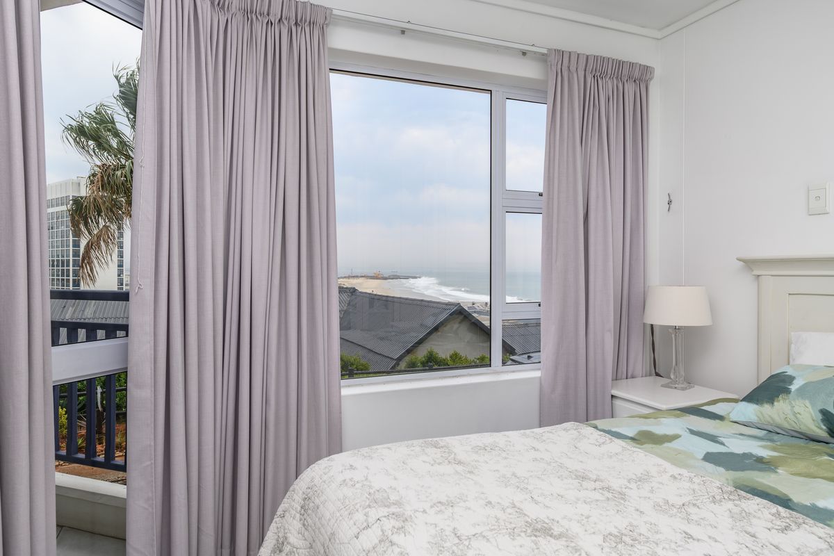 A bright bedroom featuring large windows with ocean views, neutral wall finishes, and integrated curtain tracks.