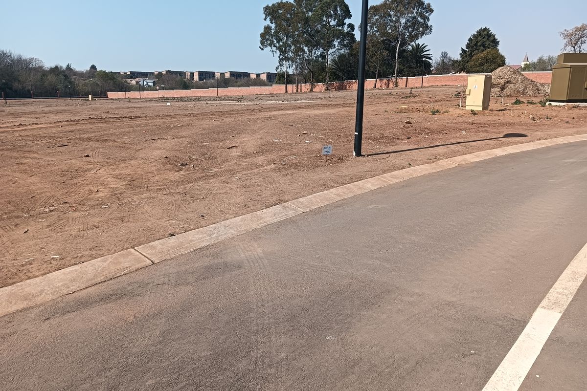 A vacant residential plot featuring a paved road frontage, concrete curbing, and established boundary walls in a developed estate setting.