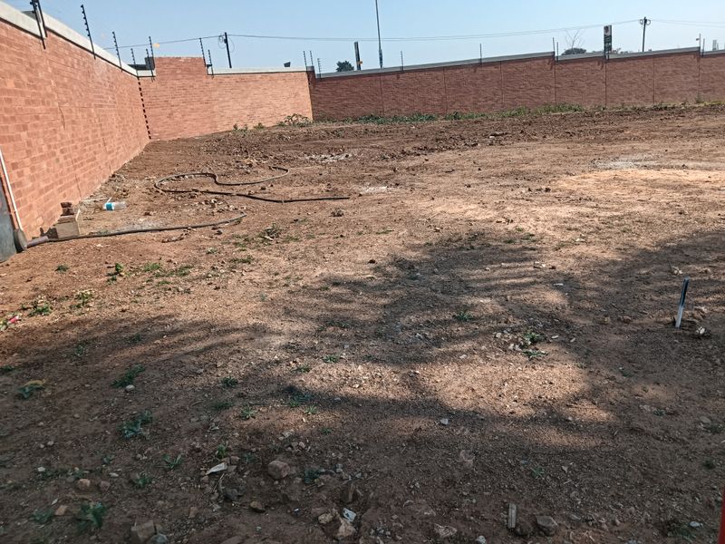 A vacant residential plot enclosed by a perimeter brick wall with installed electric fencing, ready for development.