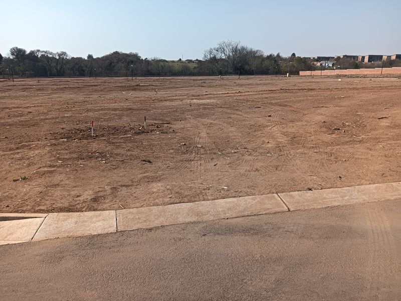 A vacant residential plot of land featuring cleared earth, boundary markers, and direct access to a paved street.