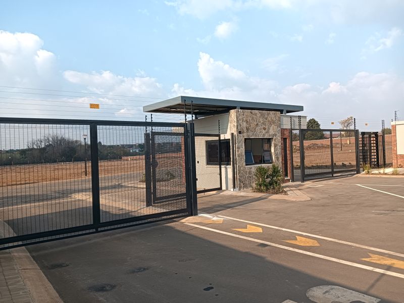 A secure residential estate entrance featuring a modern guard house with stone cladding, automated security gates, and electric fencing.
