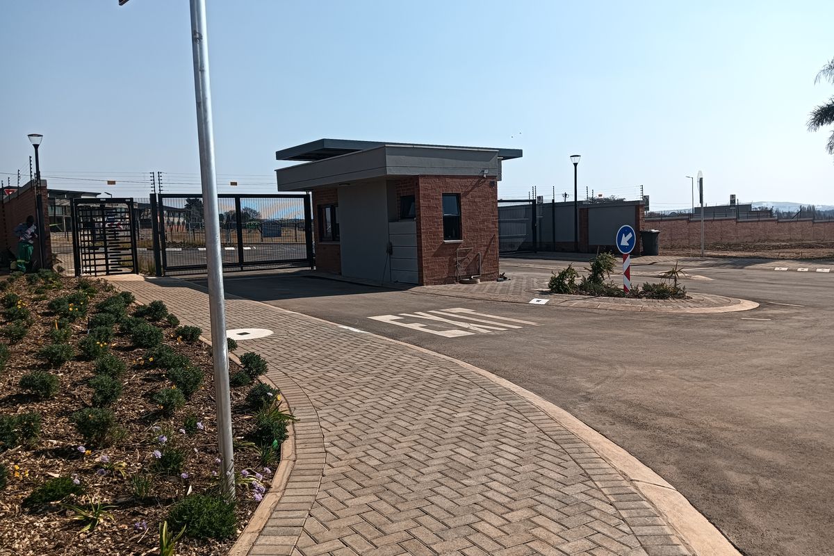 A modern residential estate entrance featuring a brick security gatehouse, paved driveway, and secure perimeter fencing.