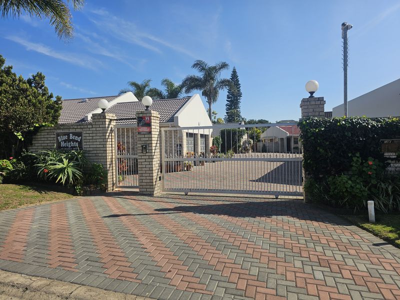 Front entrance view of Blue Bend Heights townhouse complex featuring a secure automated gate, brick paved driveway, and perimeter walling.