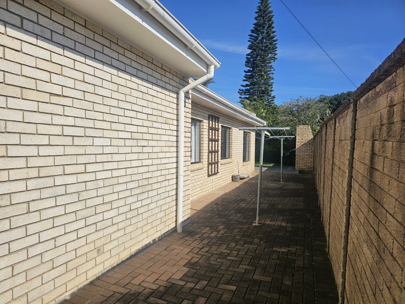 A side exterior view of the townhouse featuring a brick facade, paved walkway, and a functional clothesline area enclosed by a boundary wall.