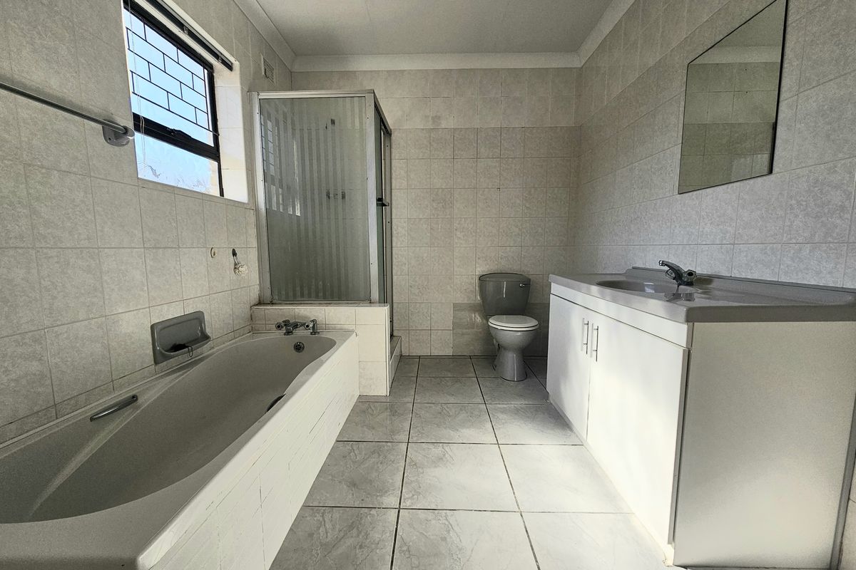 A spacious, functional bathroom featuring a built-in bathtub, separate shower enclosure, vanity basin, and toilet with neutral wall and floor tiling.