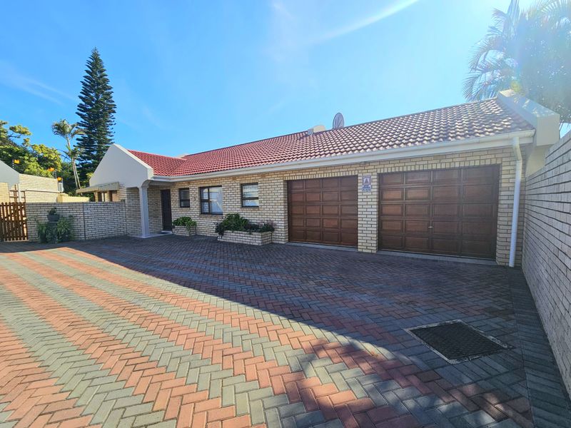 Front exterior view of a townhouse featuring a double garage, brick facade, tiled roof, and a spacious paved driveway.