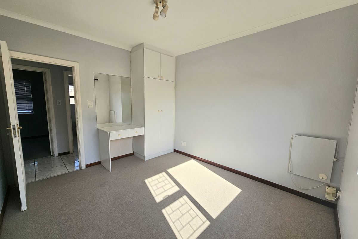 A vacant bedroom featuring neutral walls, carpet flooring, a built-in wardrobe with an integrated vanity, and a wall-mounted heater.