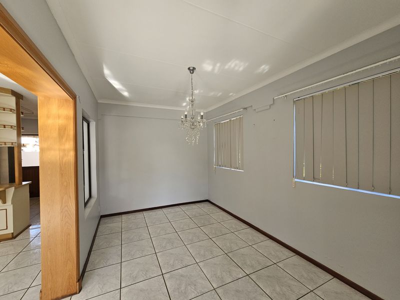 An empty dining room featuring ceramic floor tiles, a crystal chandelier, and vertical blinds, offering a blank canvas for your personal style.
