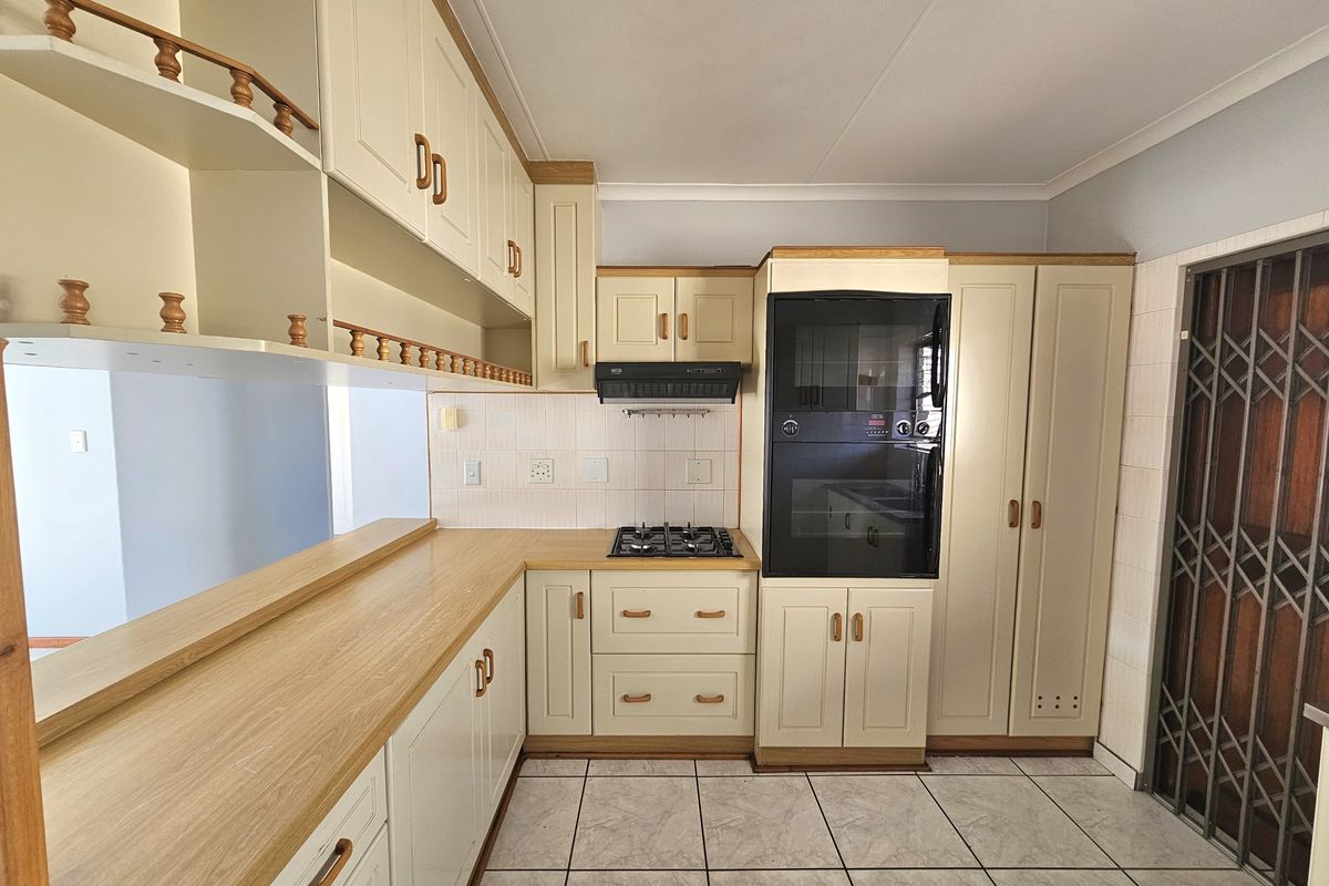 A functional kitchen featuring built-in cabinetry, laminate countertops, a gas hob, an integrated oven, and tiled flooring with a security gate entrance.