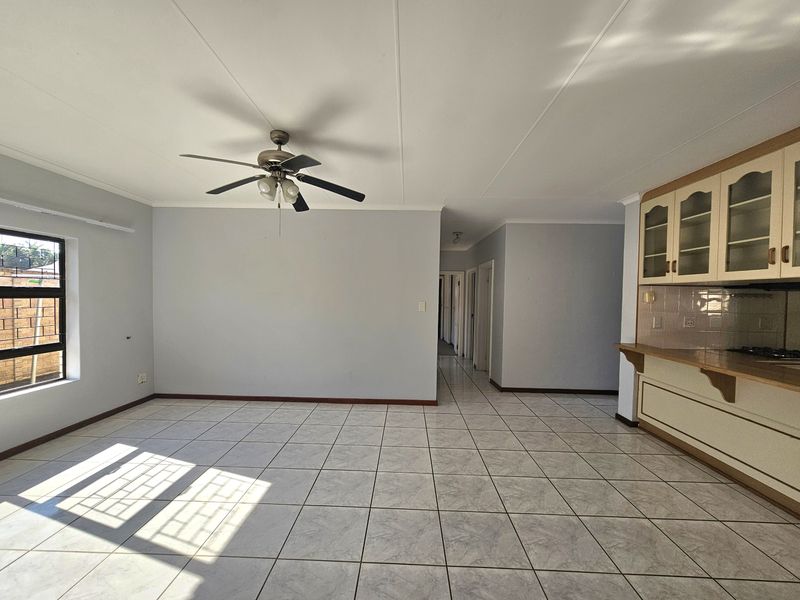 Spacious open-plan living area featuring tiled flooring, a ceiling fan, and a functional kitchen with built-in cabinetry and a breakfast counter.