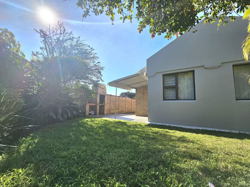 Rear garden view featuring a lawn, a covered patio area, and a built-in brick braai facility against a perimeter wall.