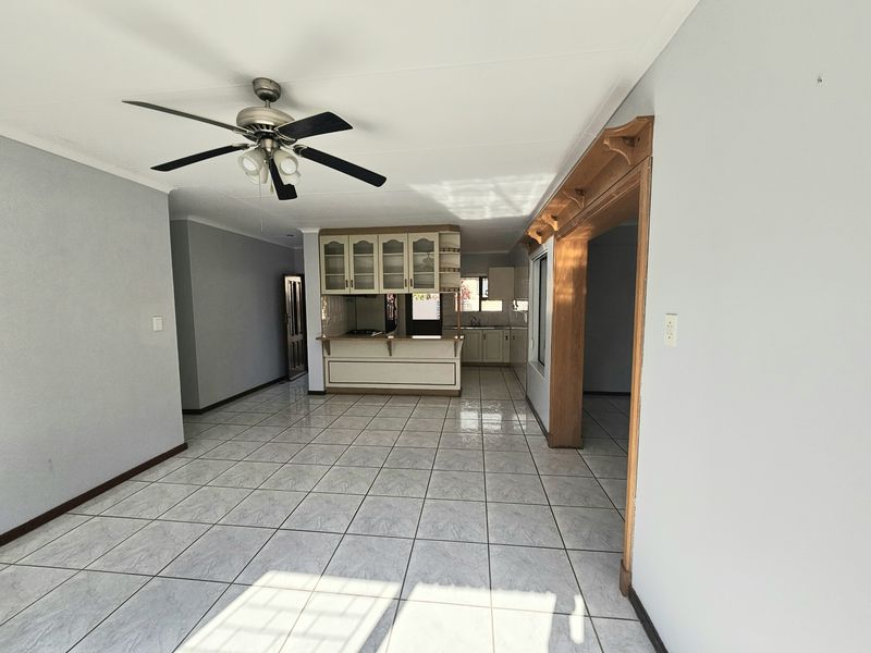 Spacious open-plan living and kitchen area featuring neutral tiled flooring, a ceiling fan, and built-in cabinetry with a breakfast counter.