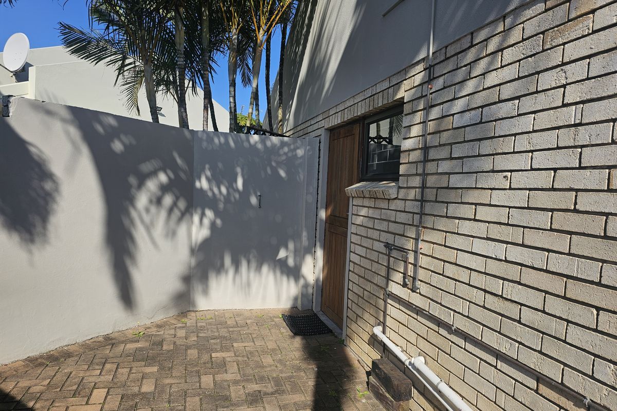A rear exterior courtyard area featuring brick paving, a face brick wall, and a timber door entrance.