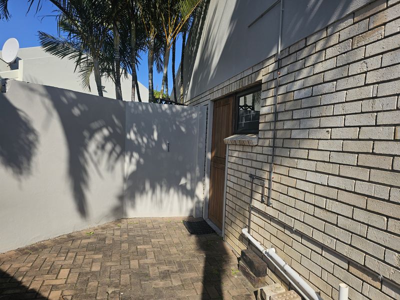 A rear exterior courtyard area featuring brick paving, a face brick wall, and a timber door entrance.