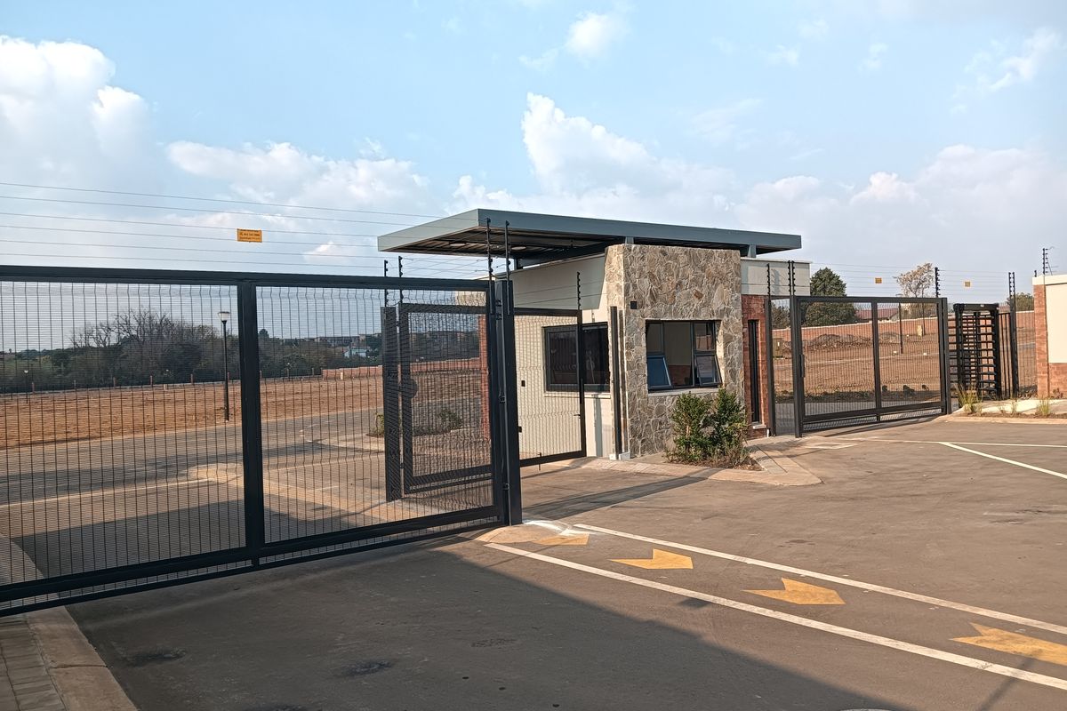 A secure residential estate entrance featuring a modern guard house with stone cladding, automated security gates, and electric fencing.