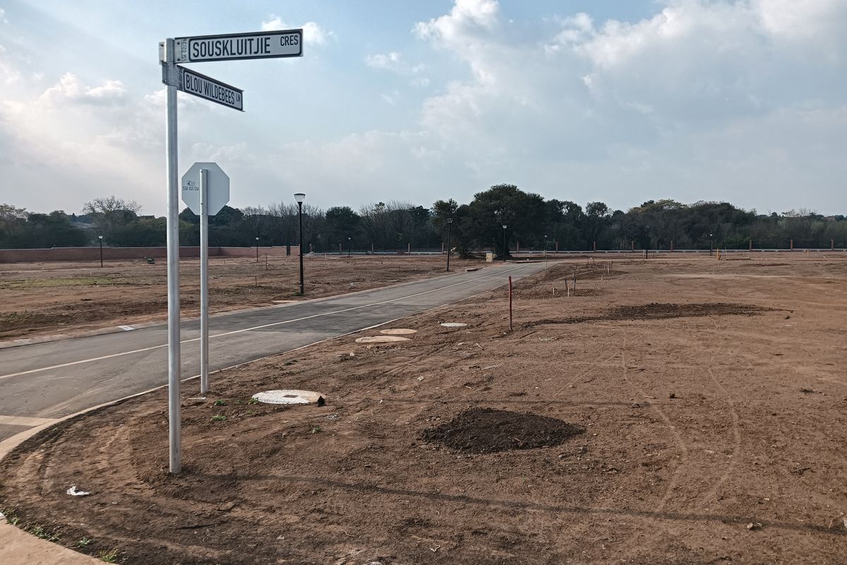 A view of a vacant residential plot featuring paved road access, street signage, and installed utility infrastructure.
