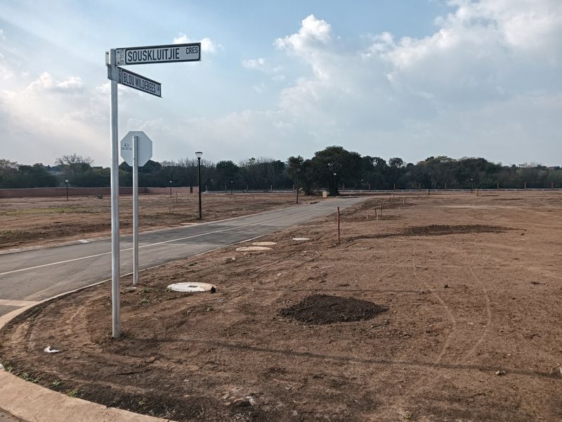 A view of a vacant residential plot featuring paved road access, street signage, and installed utility infrastructure.