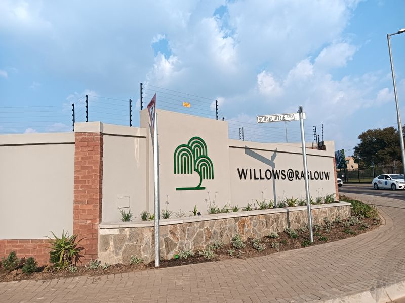 The entrance facade of Willows@Raslouw estate, featuring a modern perimeter wall with stone cladding, electric fencing, and clear street signage.