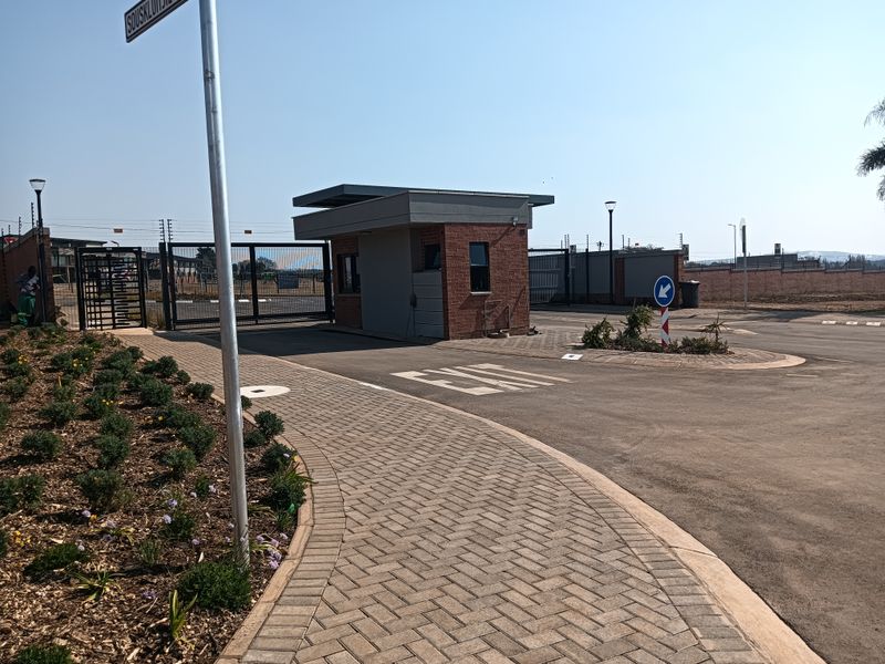 A modern residential estate entrance featuring a brick security gatehouse, paved driveway, and secure perimeter fencing.