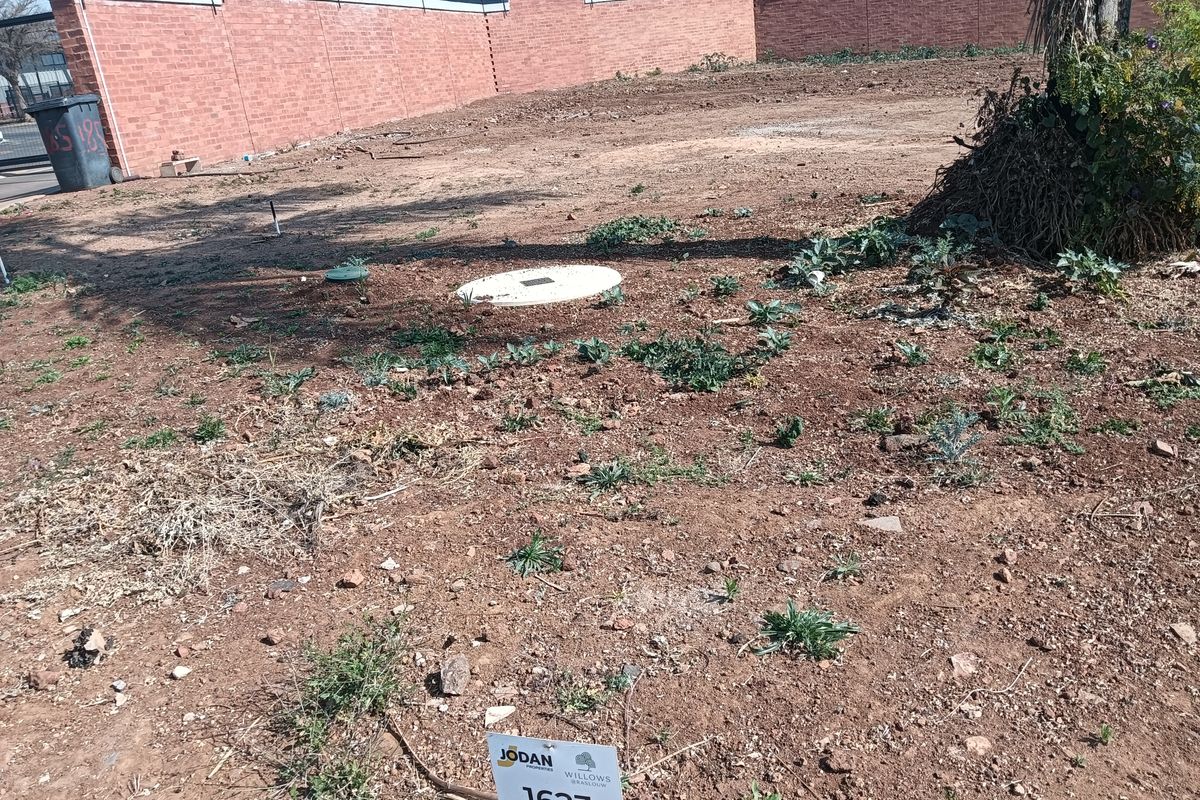 A vacant residential plot featuring a perimeter brick wall with electric fencing and a level ground surface.
