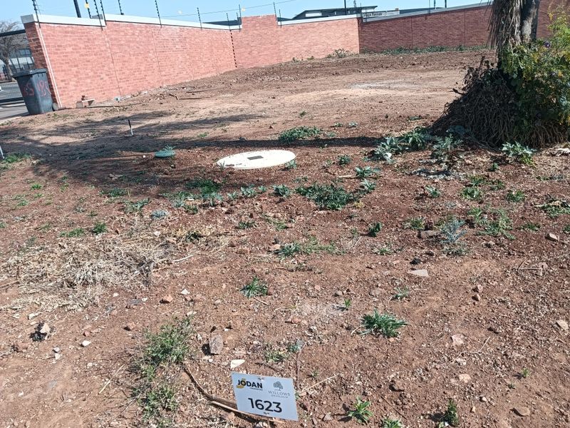 A vacant residential plot featuring a perimeter brick wall with electric fencing and a level ground surface.