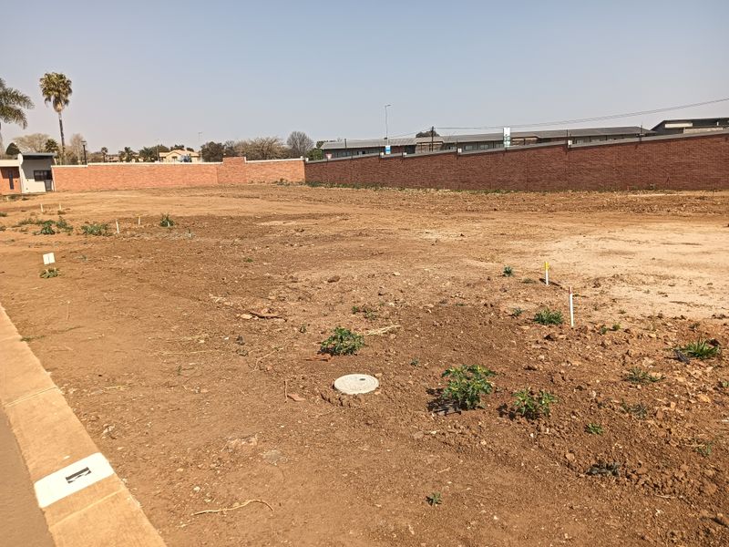 A vacant residential plot featuring a perimeter brick wall, survey markers, and utility access points, ready for development.