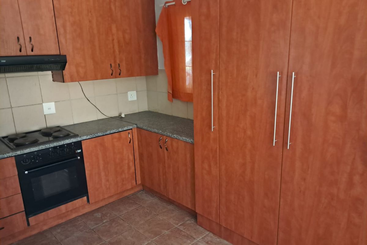 A functional kitchen featuring wood-finish cabinetry, laminate countertops, a built-in oven, and an electric hob with a tiled backsplash.