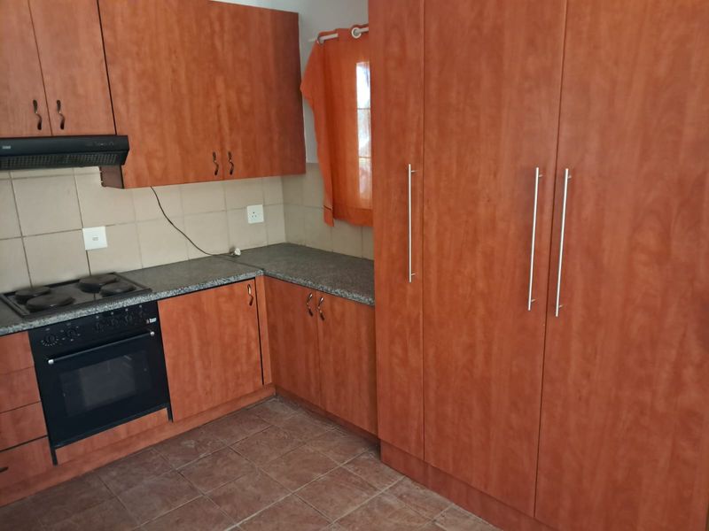 A functional kitchen featuring wood-finish cabinetry, laminate countertops, a built-in oven, and an electric hob with a tiled backsplash.