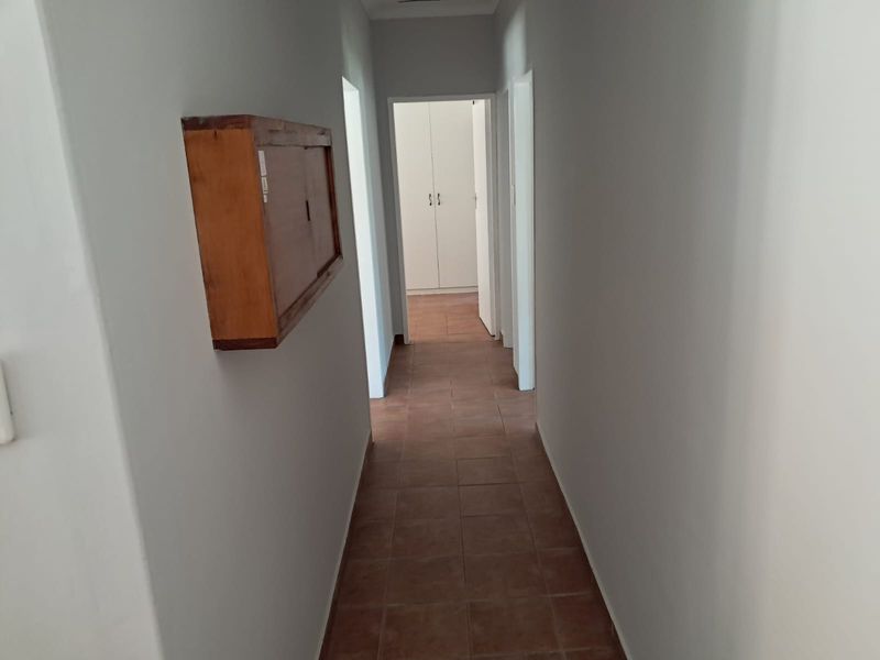 A functional hallway featuring tiled flooring and access to adjacent rooms with built-in storage cupboards visible at the end of the corridor.