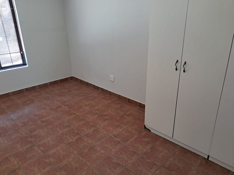 A clean, empty bedroom featuring tiled flooring, a built-in wardrobe, and venetian blinds on the window.