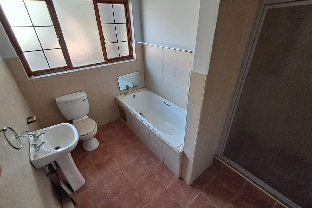 A functional bathroom featuring a pedestal basin, toilet, built-in bathtub, and a separate shower enclosure with tiled finishes throughout.