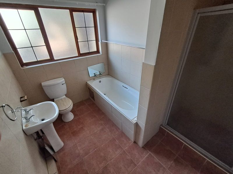 A functional bathroom featuring a pedestal basin, toilet, built-in bathtub, and a separate shower enclosure with tiled finishes throughout.