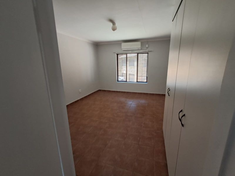 An empty bedroom featuring tiled flooring, built-in cupboards, and a wall-mounted air conditioning unit.