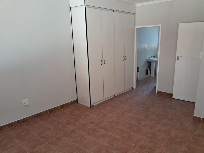 A clean, empty bedroom featuring tiled flooring, built-in cupboards, and direct access to an en-suite bathroom.