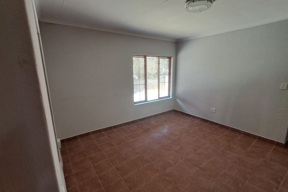 A clean, empty bedroom featuring neutral walls, tiled flooring, and a window fitted with venetian blinds.