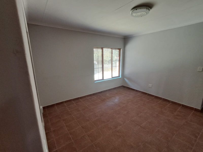 A clean, empty bedroom featuring neutral walls, tiled flooring, and a window fitted with venetian blinds.