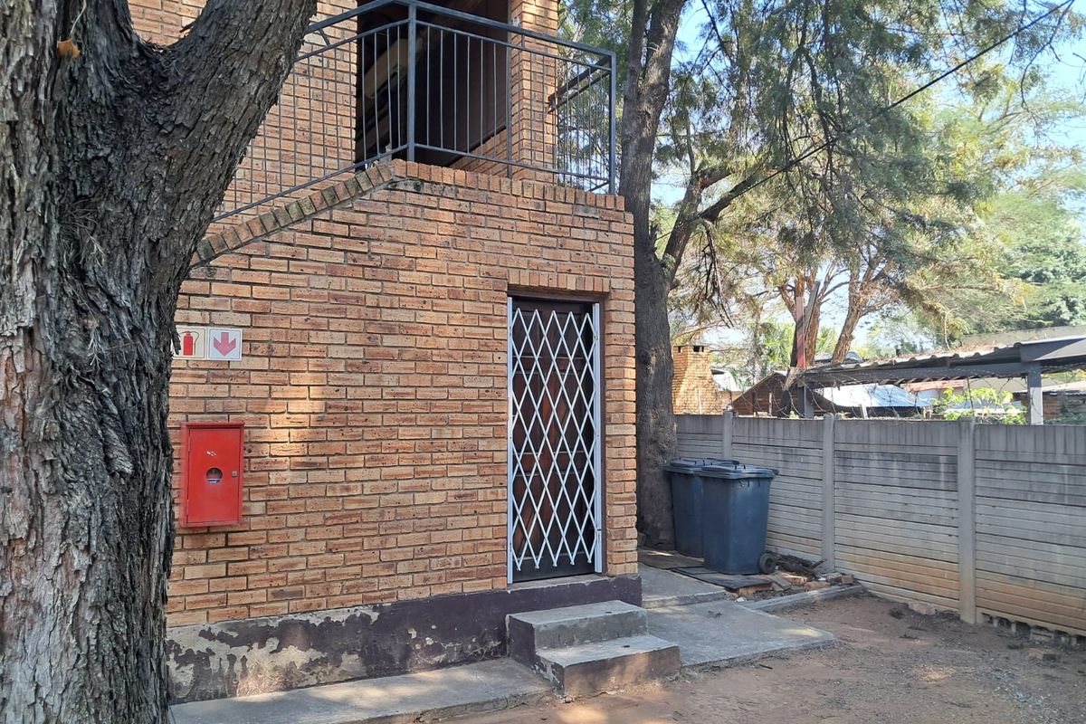 Rear exterior view of a face brick apartment building featuring a metal security gate, balcony railing, and concrete steps.