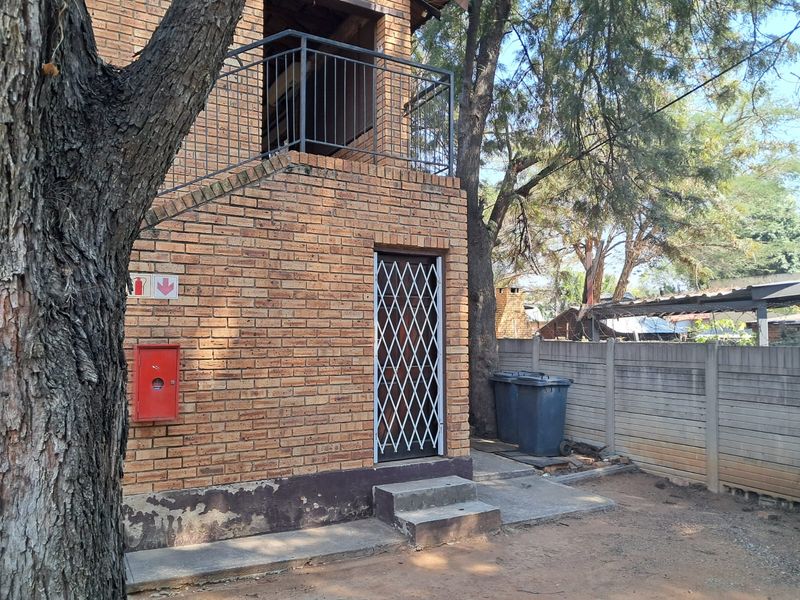 Rear exterior view of a face brick apartment building featuring a metal security gate, balcony railing, and concrete steps.