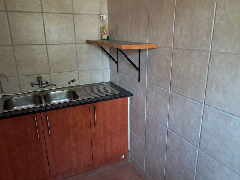 A functional scullery area featuring a stainless steel double sink, laminate countertop, built-in cabinetry, and tiled walls.